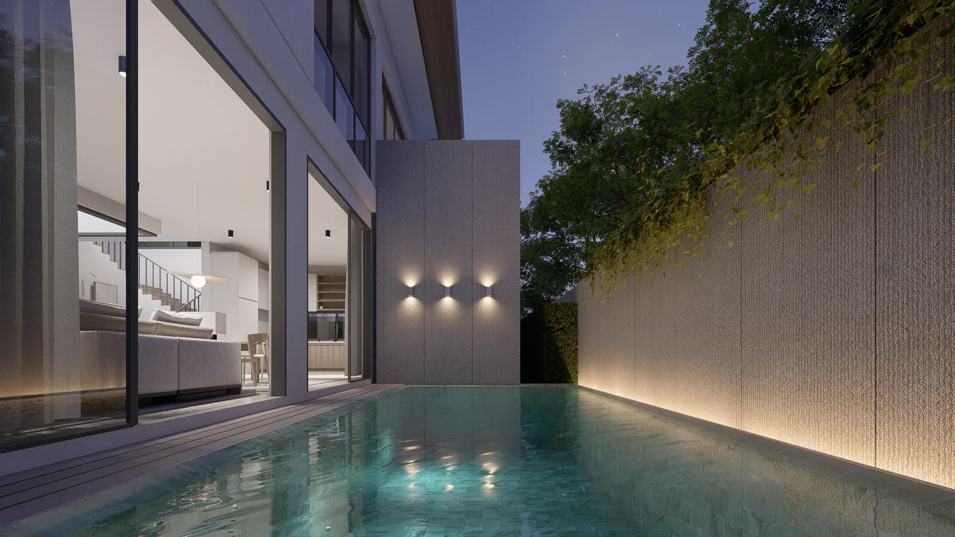 Evening pool view showing the glazed shared spaces, solid side wall and controlled exterior lighting.