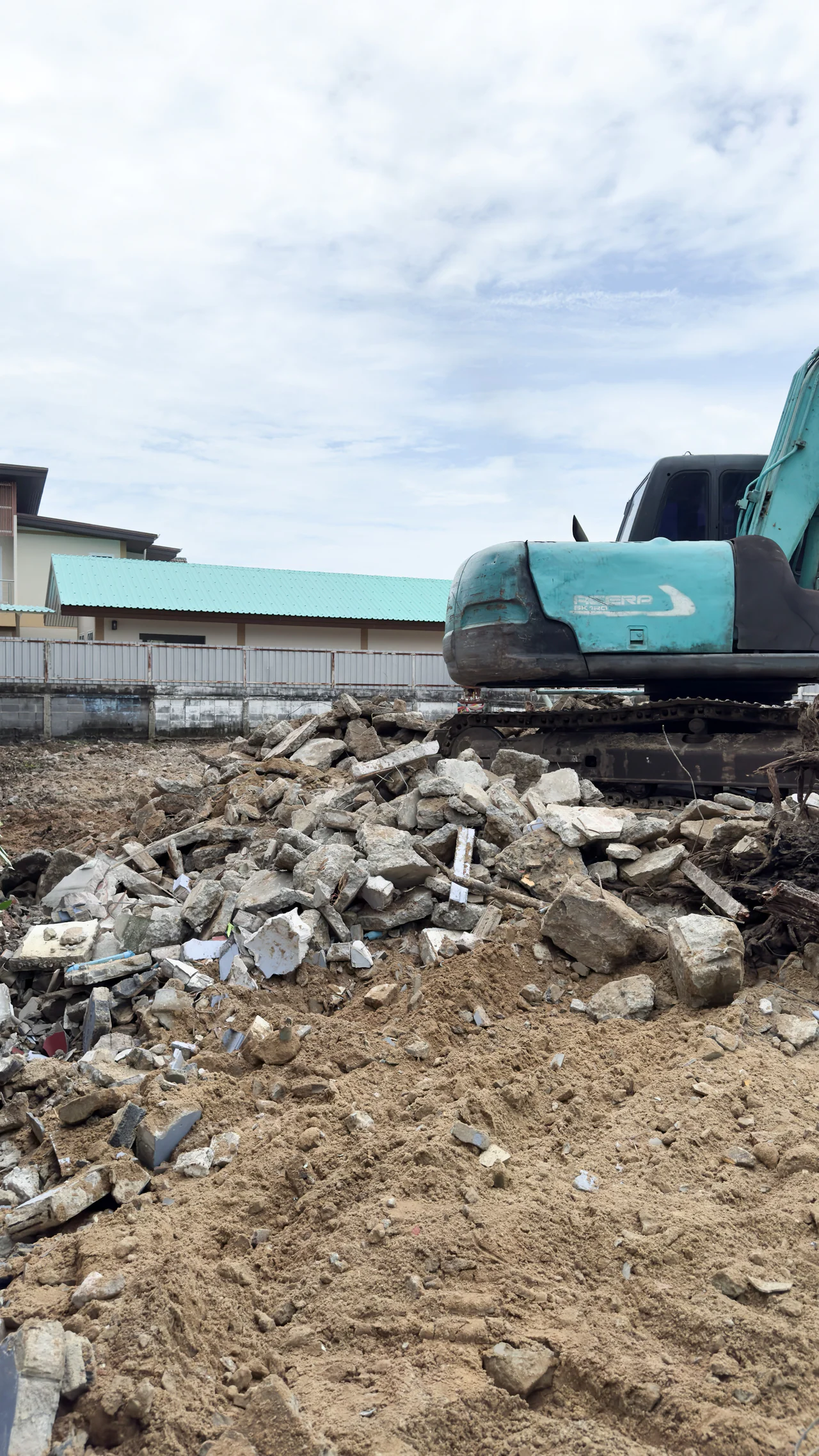 Demolition-stage photograph of rubble and an excavator at the SUKHUMVIT 105 site.