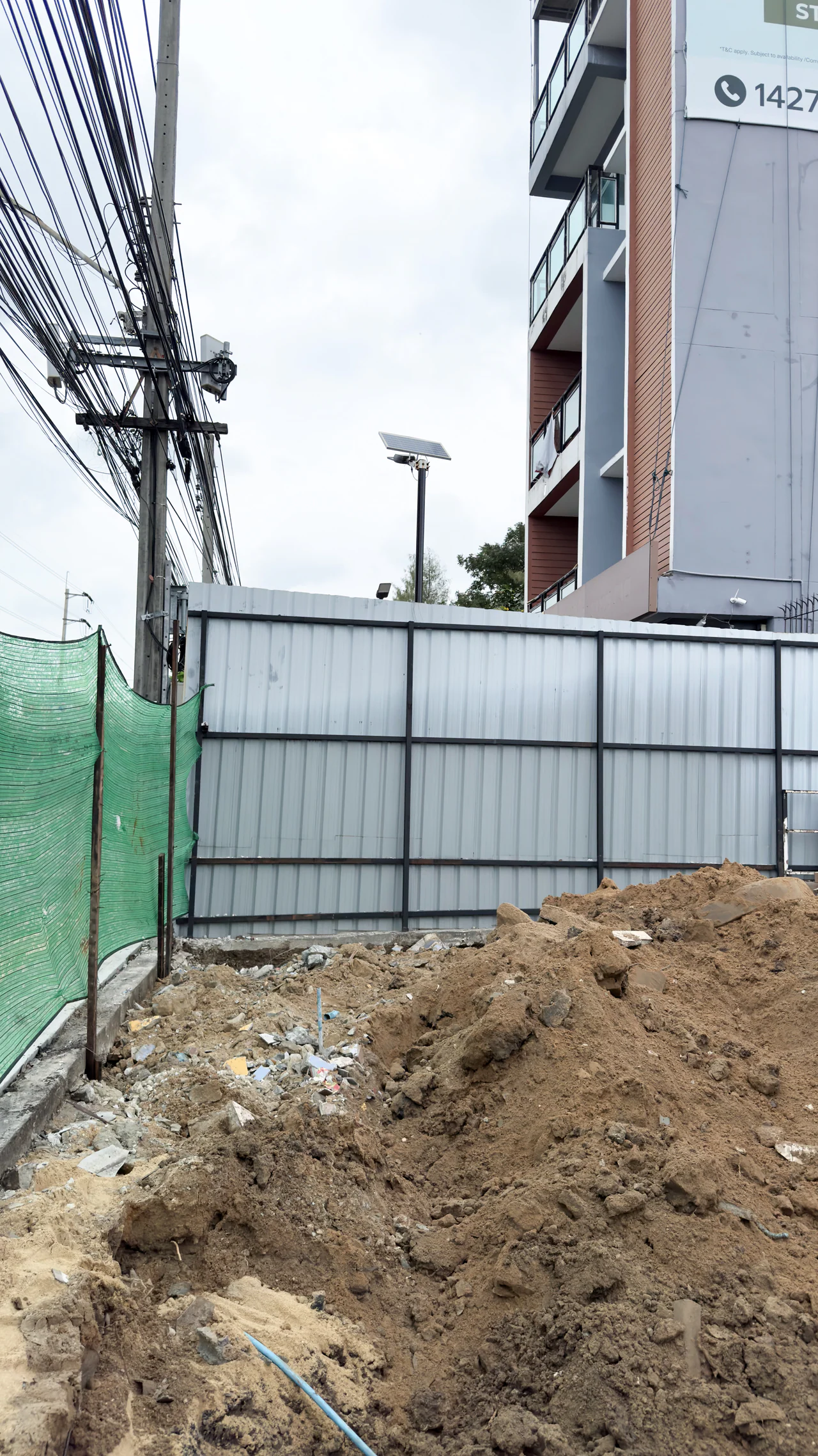 Demolition-stage photograph of soil, temporary fencing and overhead utility lines beside the neighbouring building.